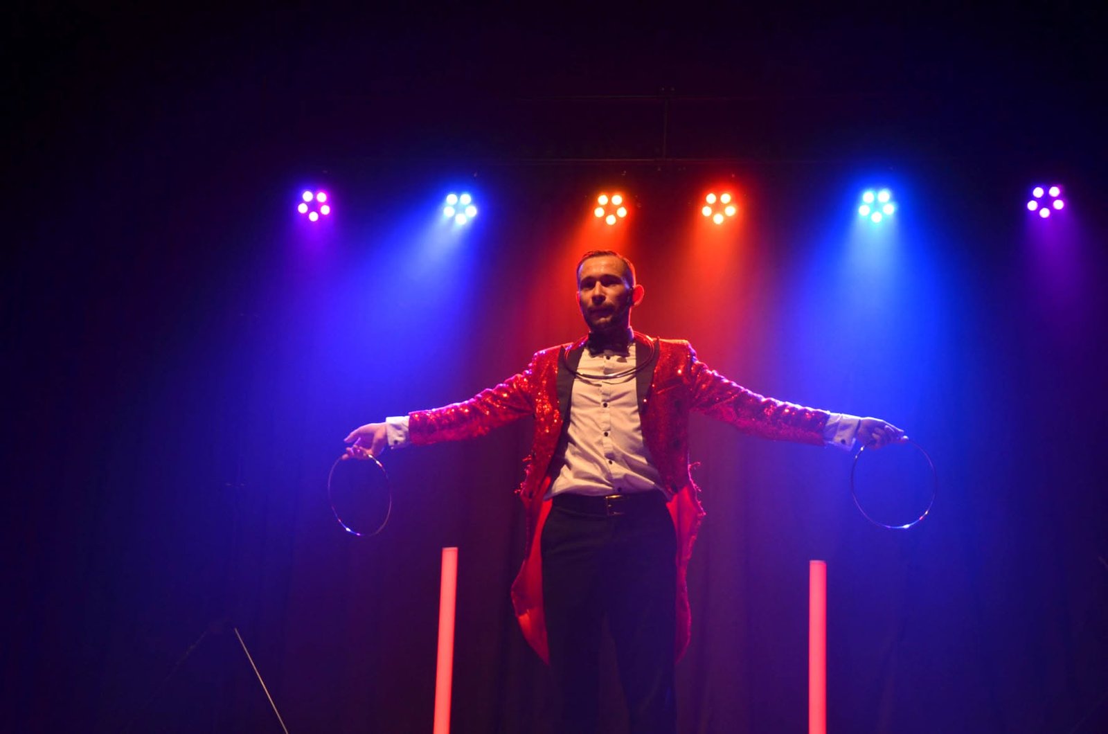 Tinou en veste rouge, les bras ouverts sous les projecteurs bleus et roses